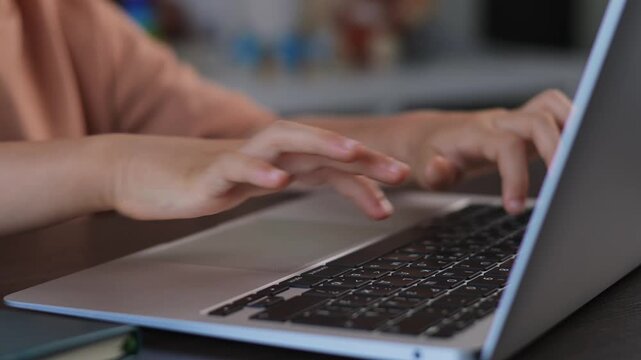 Child hands using laptop computer for education at home desk. Computer enables online classes, digital coursework and learning tasks while typing on keyboard illustrates modern study environment. 