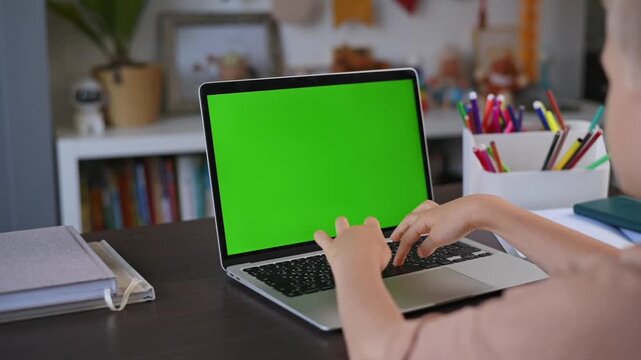 Child typing on laptop keyboard computer with green screen in home workspace. Computer device with chroma key helps create education templates, business visuals, online learning concepts, digital 