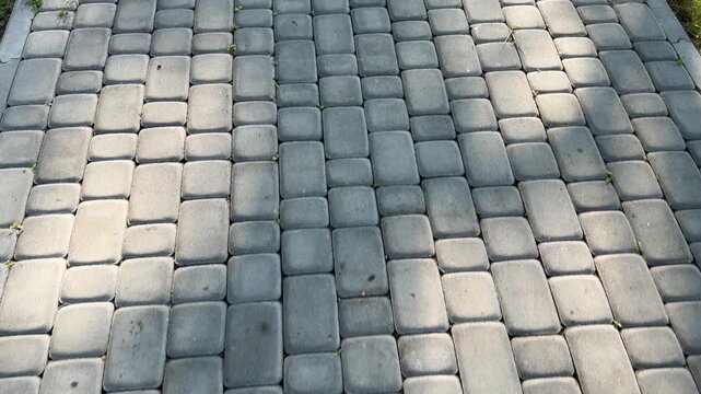 camera moves forward above neatly laid gray paving stones, capturing the texture, pattern, and steady walking motion along a well maintained pedestrian pathway. First person view.