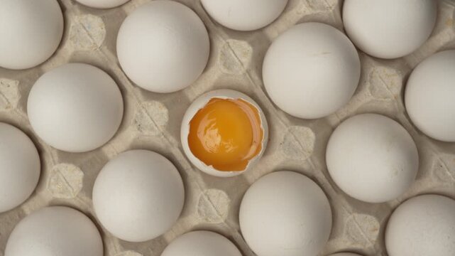 Close-up of raw chicken organic eggs in egg cardboard box. One egg cracked showing the yolk.