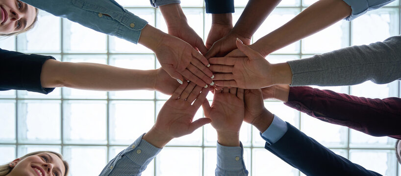 Overhead view of hands stacked together in a circle, representing teamwork, unity and shared commitment among colleagues