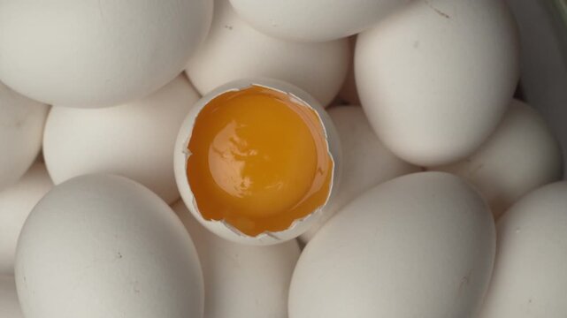 Close-up of raw chicken organic eggs in egg cardboard box, top view. One egg cracked showing the yolk.