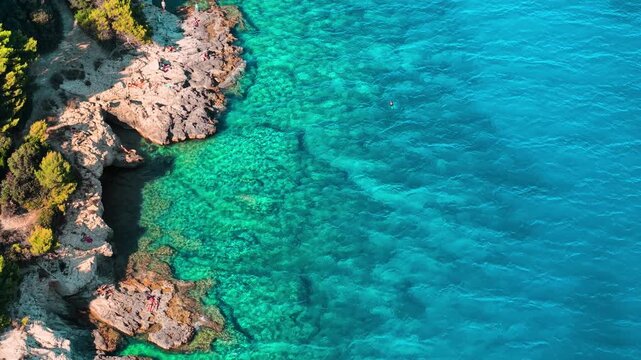 Drone top view of a rugged rocky shoreline meeting the transparent turquoise waters of the Adriatic Sea in Pula, Croatia