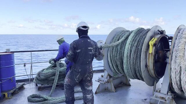 Maritime workers uncoiling lines from shipboard winch drums.