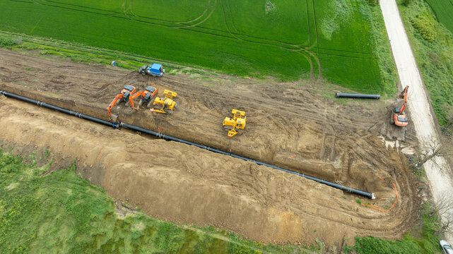 Aerial view of a major pipeline construction project. Heavy machinery including excavators and pipelayers install a new gas line in a rural field. Industrial energy infrastructure development.
