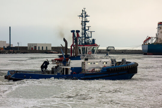 Powerful ice-breaking tugboat at work in a frozen harbor, navigating through icy waters to assist a cargo ship. A scene of maritime industry and winter logistics.