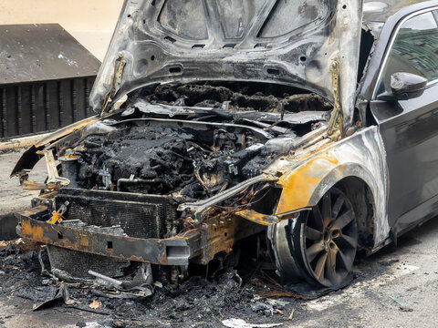 Burnt Car with Severe Fire Damage and Open Hood on a City Street. Charred Engine, Soot, and Melted Parts. Concept for Insurance Claim and Arson.