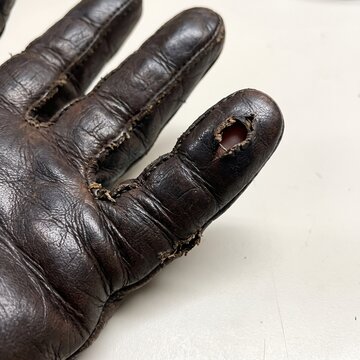 A leather work glove worn through at the fingertip as a hard-work and endurance metaphor