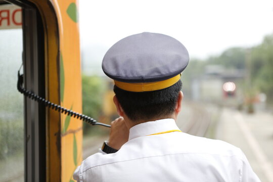 A train conductor holding a transceiver monitors the railway platform.