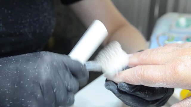 Close-up of a professional nail technician using a manual nail file to remove old gel polish from a client's fingernail before a new manicure. Nail care, manicure preparation.