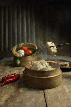 Steaming dumplings lifted with chopsticks over bamboo steamer in rustic setting
