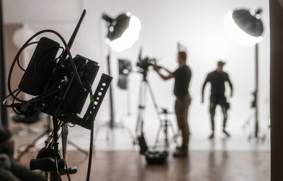 Silhouetted figures of a film crew working under professional studio lighting with camera equipment. Concept of filmmaking, media production, and backstage work environments.