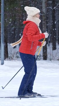 Side view of a dedicated female skier practicing classic cross country skiing in a beautiful snowy forest, gliding on a trail while snowflakes fall during a winter workout for a healthy lifestyle