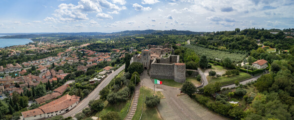 The entrance side of Padenghe Castle faces a drone panorama of converging roads, olive groves and the Lake Garda town below. © Artem