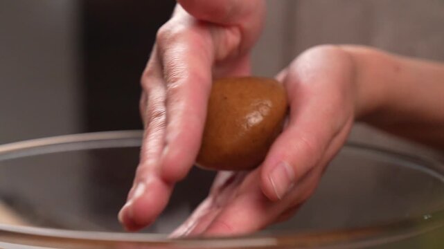Close-up of a pastry chef's hands rolling cookie dough balls.