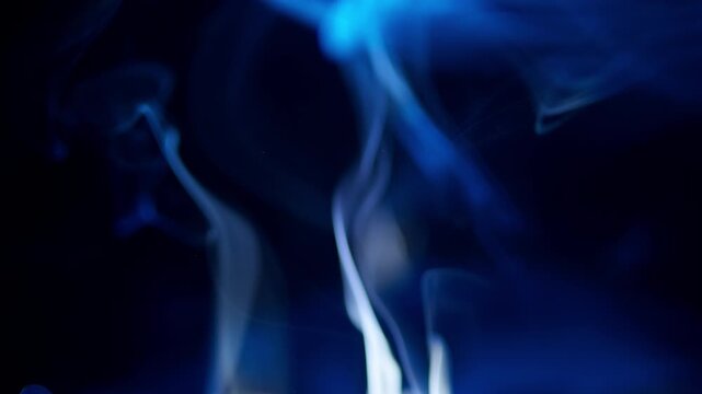 Abstract blue smoke gracefully rising and swirling on a deep dark background, creating an ethereal and mysterious visual. This flowing vapor provides a versatile texture and overlay element for