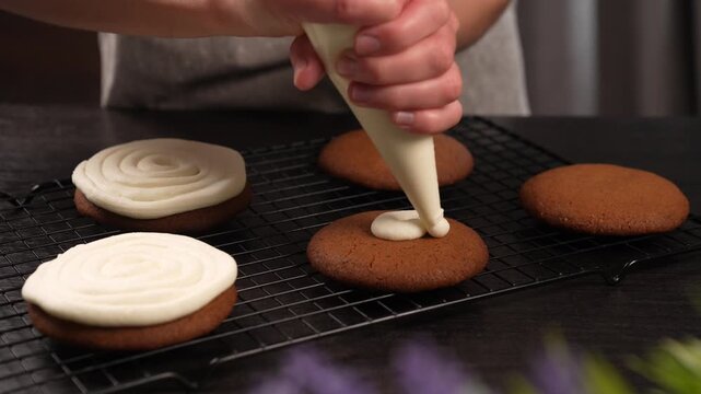 Close-up of hands squeezing cream from a pastry bag onto a cookie (slow motion).