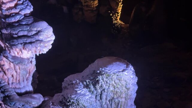 Stalactite and stalagmite formations inside a dark cave. Geological mineral structures illuminated by light. Underground nature explore for earth science study.