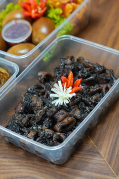 Close up of cumi hitam, Indonesian squid cooked in rich black ink sauce with spices, served in plastic container, authentic seafood and exotic Asian cuisine concept