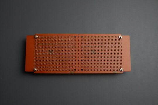 A brown perforated electronic prototype circuit board, or perfboard, is laid flat against a dark gray background.