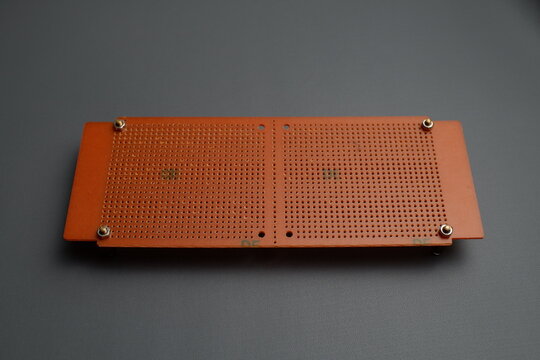 A brown perforated electronic prototype circuit board, or perfboard, is laid flat against a dark gray background.