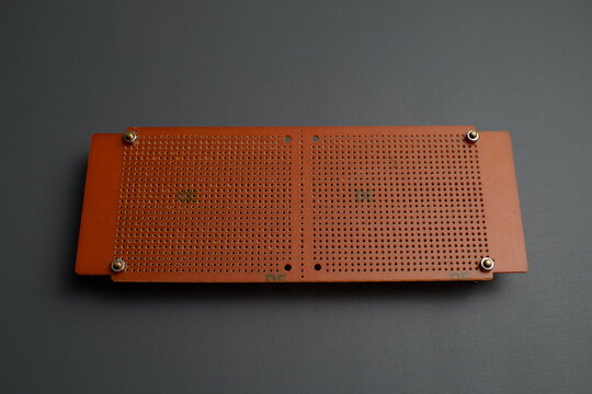 A brown perforated electronic prototype circuit board, or perfboard, is laid flat against a dark gray background.