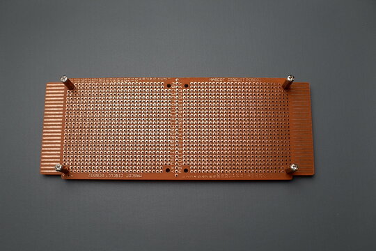A brown perforated electronic prototype circuit board, or perfboard, is laid flat against a dark gray background.