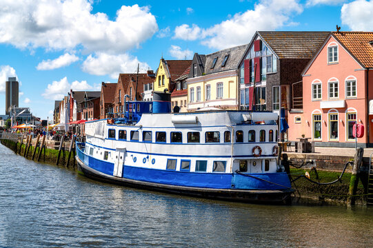 Moored restaurant ship in Husum's historic inner harbor with colorful gabled houses along the waterfront on a sunny summer day.