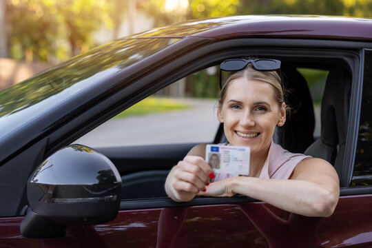 Happy woman showing driving license from car window after passing driving test