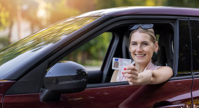 Happy woman showing driving license from car window after passing driving test. banner with copy space