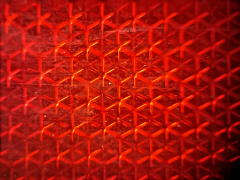 Abstract close-up background texture of a red safety vehicle reflector with a honeycombed geometric pattern.