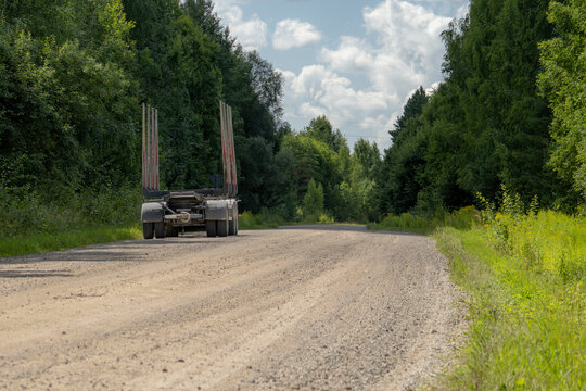 Empty logging trailer parked on a gravel road through a green summer forest