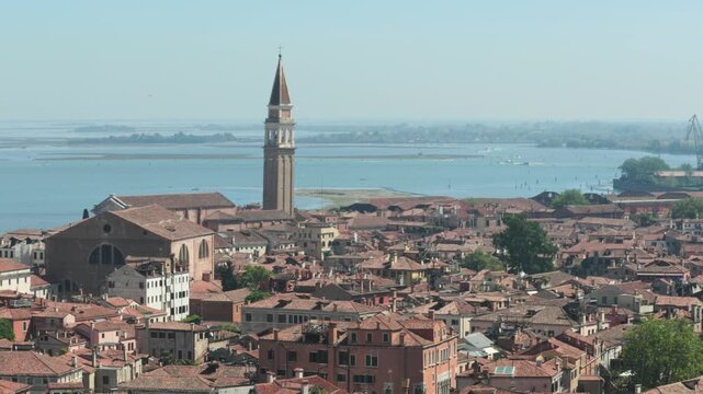 Historic terracotta rooftops and a leaning bell tower stand before the shimmering blue lagoon. This expansive urban landscape inspires summer travel and appreciation for ancient Italian heritage.