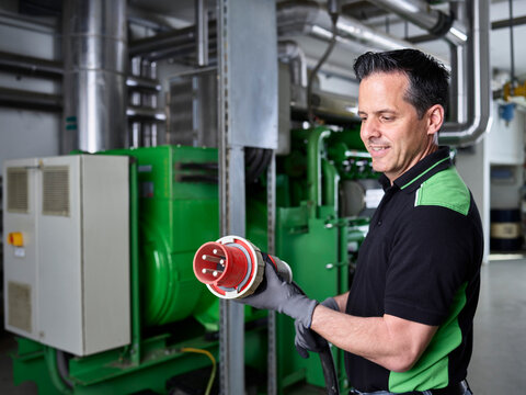 Combined heat and power plant, worker holding high current plug