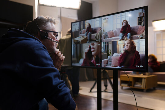 A male director watches an actress on a playback monitor backstage