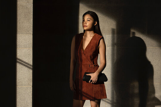 Woman holding clutch bag while standing in front of wall