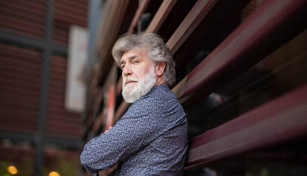 Mature man with white beard looking away while standing in front of metal wall