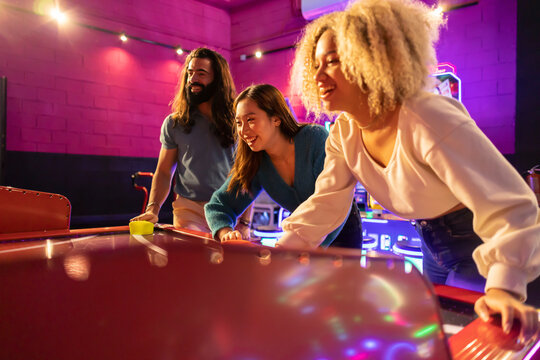 Happy friends having fun playing air hockey at amusement arcade