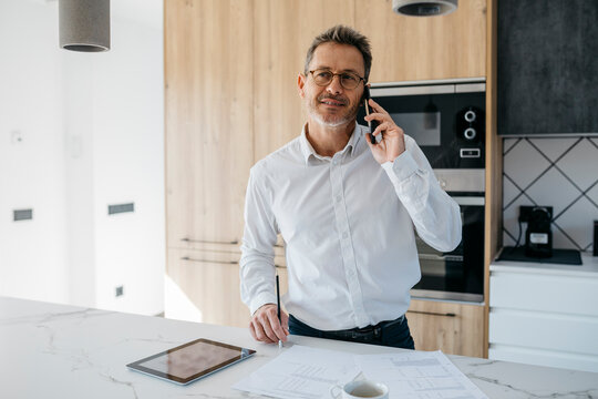 Male professional looking away while talking on mobile phone in domestic kitchen