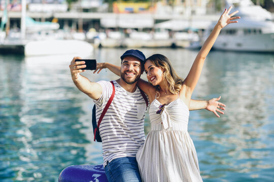 Spain, Andalusia, Malaga, happy tourist couple taking selfie with smartphone at the harbor