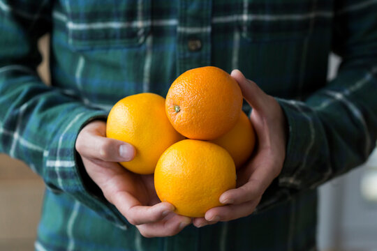 Man's hands holding four oranges, close-up