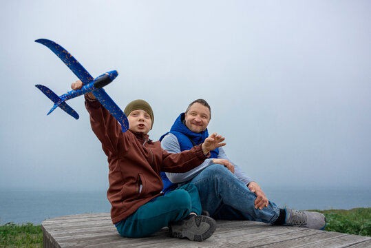 A father and son play with a toy airplane outdoors in the park