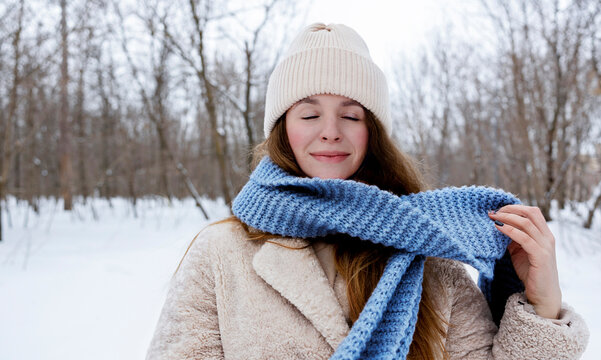 Young smiling woman with eyes closed wearing blue scarf in winter forest