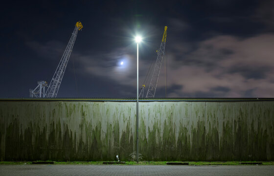 Netherlands, South Holland, Rotterdam, Old harbor cranes seen from behind surrounding wall at night