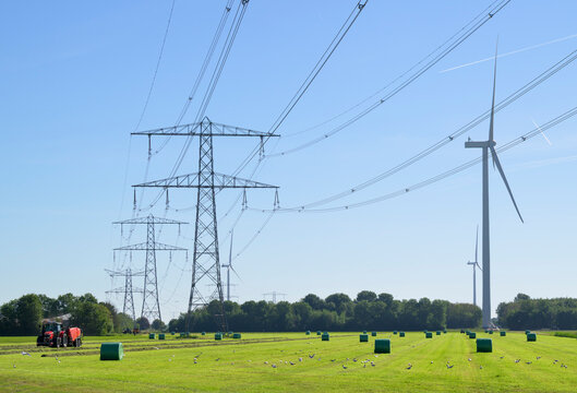 Tractor cuts grass near a wind turbine and power line in Flevopolder