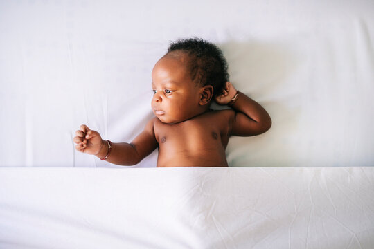 Cute shirtless baby boy lying on bed under sheet at home