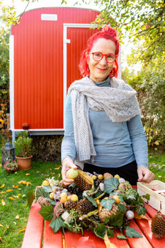 Portrait of smiling senior woman with red dyed hair tinkering autumnal decoration in the garden