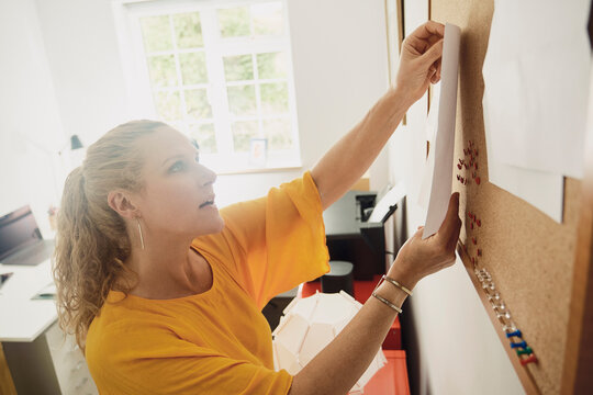 Woman pins a paper to a noticeboard in her home office