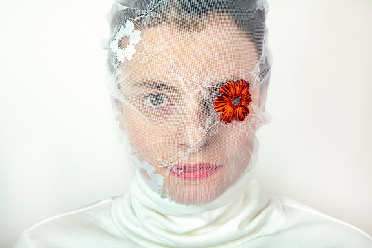 Portrait of young woman wearing white veil with flower covering one eye