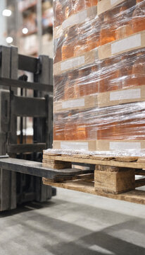 Wrapped pallet being lifted by a forklift in a warehouse aisle. The image shows palletized boxes secured with stretch wrap on wooden pallet ready for storage or shipping.